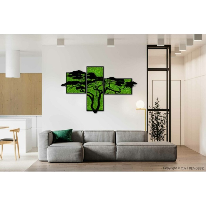 Een moderne woonkamer met minimalistische inrichting. Een grote grijze sectionele bank is versierd met groene en witte kussens. Boven de bank is een BEMOSS-mosschilderij met meerdere panelen gecentreerd, wat een vleugje natuur toevoegt. De ruimte is voorzien van lichte houtaccenten en witte muren, met uitzicht op een keuken.