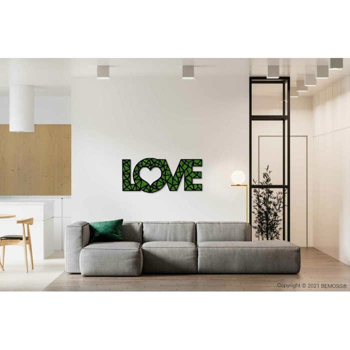 Een moderne woonkamer is voorzien van een lichtgrijze sofa met een groen kussen. Op de muur boven de bank staat 'LOVE' met een hartvormige 'O' en een groen geometrisch patroon. Daaronder voegt een BEMOSS-mosschilderij een natuurlijke textuur toe aan de strakke, minimalistische ruimte, die een wit en houten thema heeft.