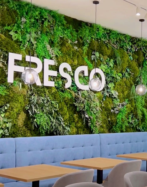 Een modern café-interieur met een grote groene BEMOSS-mosschilderij met het woord 