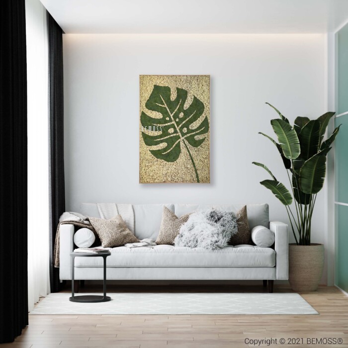Een moderne woonkamer met een witte bank versierd met neutrale kussens en een donzige grijze plaid. Naast de bank staan een grote potplant en een bijzettafel. Hierboven voegt een Earth Gagos met een levendig groen blad een organisch tintje toe aan de ongerepte witte muur.