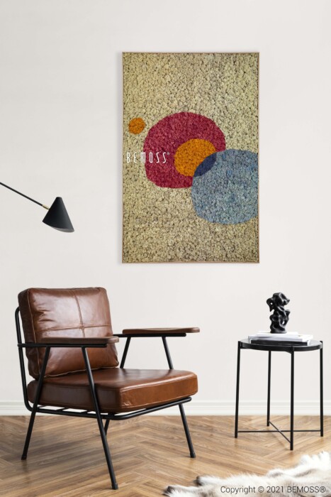 In een moderne woonkamer staat een bruinleren stoel met een zwart metalen frame, een zwarte vloerlamp en een klein zwart bijzettafeltje met een decoratief item. Aan de muur wordt een abstracte Oleiros getoond naast gestructureerde kunstwerken met overlappende cirkels in rood, blauw en oranje.