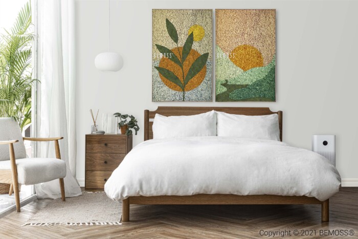 Een moderne slaapkamer is voorzien van een houten bed met wit beddengoed, een nachtkastje met een lamp en een klok, en twee abstracte kunstwerken met een natuurthema boven het bed. In de hoek staan een grijze fauteuil en een potplant, aangevuld met een abstracte moraal aan de muur, waarbij natuurlijk licht door een nabijgelegen raam stroomt.