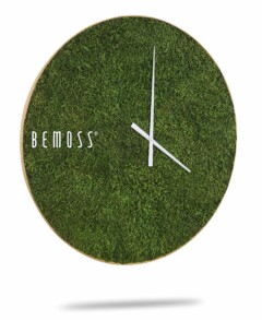 Een ronde wandklok met een groene grasachtige textuur als achtergrond. Het beschikt over minimalistische witte uren- en minutenwijzers, zonder cijfers. Op de linkerkant van de wijzerplaat staat in witte letters het woord "Mos klok FLATMOSS" gedrukt, wat doet denken aan een serene mosschilderij.