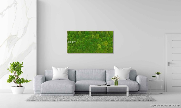 Een minimalistische woonkamer is voorzien van een lichtgrijze bank met witte kussens, een kleine salontafel met een bloemstuk en potplanten. Boven de bank hangt een groene Mosschilderij BEMOSS® ORTHO FOREST als een opvallend kunstwerk. De kamer heeft witte muren en een witte deur.