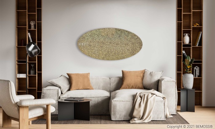 Een moderne woonkamer met een lichtgrijze bank met beige en bruine kussens, een lichte deken en twee zwarte bijzettafels. De achtergrond heeft ingebouwde houten planken met decoritems, een ovale muurkunst en een opvallende Mosschilderij Ellips RENDIERMOS mono. Links staat een grijze stoel.