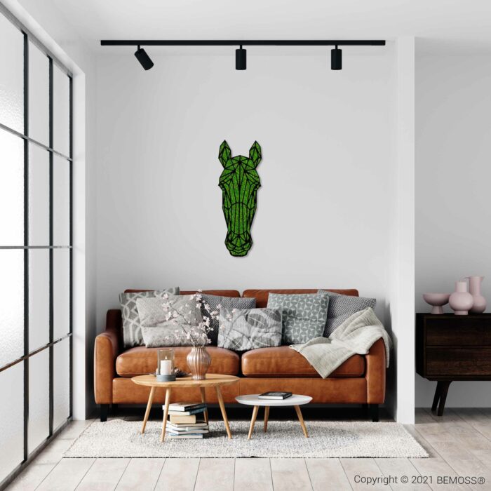 Een moderne woonkamer met een bruinleren bank versierd met kussens met verschillende patronen. Boven de bank hangt een geometrisch kunstwerk van een paardenhoofd aan een witte muur naast een levendige moswand van BEMOSS. Voor de bank staat een houten salontafel met decor, terwijl een bijzettafel en ramen zichtbaar zijn.