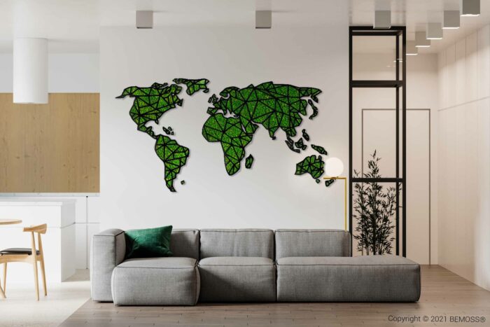 Moderne woonkamer met een grijze bank en groen kussen op de voorgrond. Aan de muur boven de bank hangt een decoratieve wereldkaart gemaakt van groene geometrische vormen, die lijkt op een BEMOSS-mosschilderij. De achtergrond omvat een eethoek met houten elementen en een plant zichtbaar door een glazen scheidingswand.