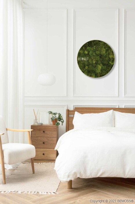 Een minimalistische slaapkamer is voorzien van een wit bed met houten hoofdeinde en bijzettafels, een witte fauteuil en een ronde groene Mosschilderij cirkel BEMOSS® ORTHO TORRES boven het bed met de tekst 
