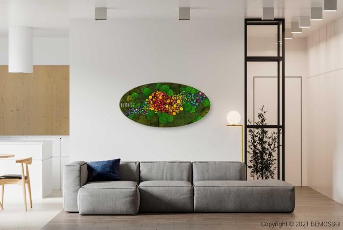 Moderne woonkamer met een grijze zitbank, een blauw sierkussen en kunst aan de muur met een kleurrijk, ovaalvormig bloemstuk. Op de achtergrond zijn een eethoek en een keuken zichtbaar. Bij de rechtermuur staat een minimalistisch zwart frame met een plant. De ruimte wordt opgefleurd door een Mosschilderij Ellips PLANTEN Mesia die textuur aan het decor toevoegt.
