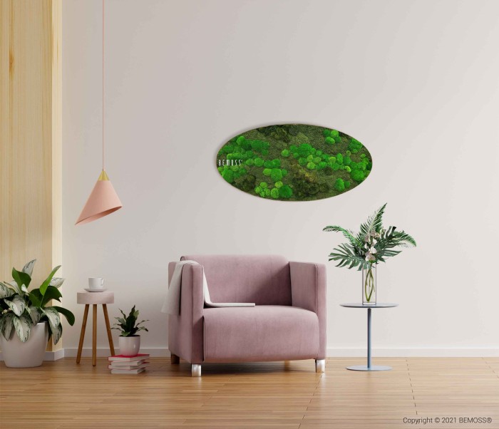 Een gezellige kamer met een lichtpaarse fauteuil, vergezeld van een klein bijzettafeltje met een plant en een koffiekopje. Boven de stoel hangt een ovaalvormige Mosschilderij Ellips BOLMOSS DUO Natural Green. De kamer is licht, met lichtgekleurde muren en nog een plant op de vloer.