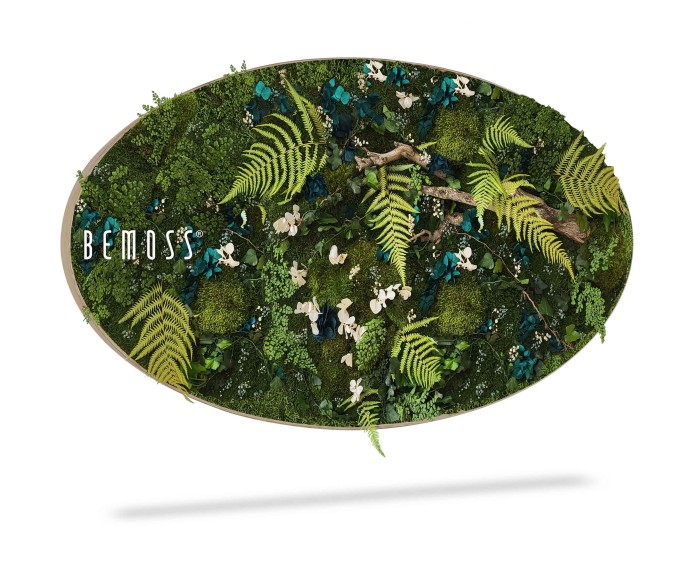 Een ovaalvormig decoratief wandstuk met een scala aan geconserveerd mos, varens en divers groen. Enkele witte bloemen en blauwe elementen worden afgewisseld tussen het gebladerte. Op de linkerkant van de moswand staat het woord 