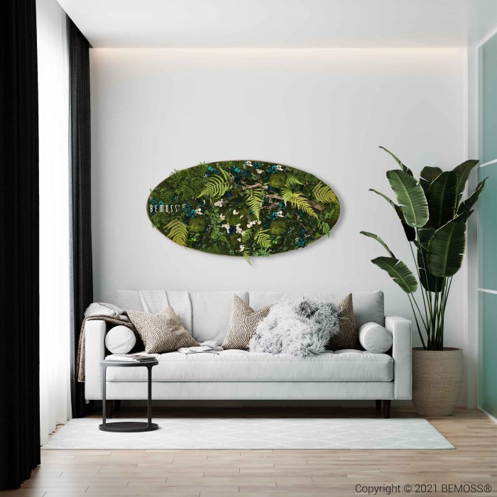 Een moderne woonkamer is voorzien van een witte bank met verschillende kussens tegen een witte muur. Boven de bank hangt een kunstwerk van de BEMOSS moschilderij. Rechts staat naast de bank een hoge kamerplant. De kamer heeft een strak, minimalistisch ontwerp met houten vloeren.