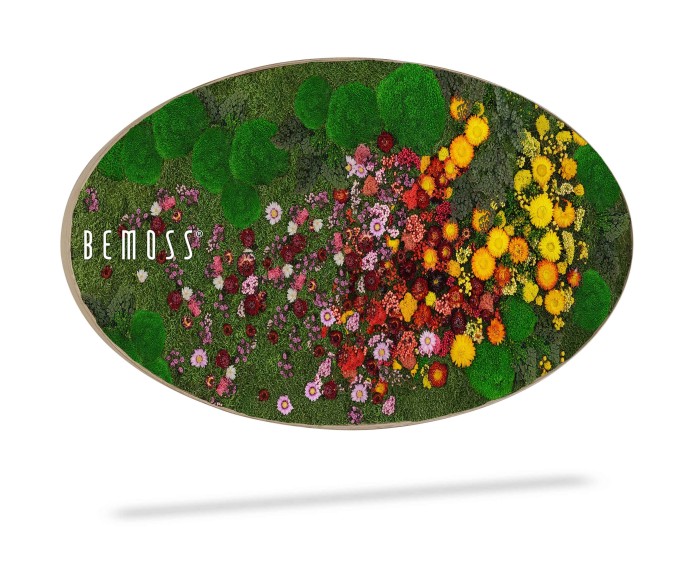 Een ovaalvormig decoratiestuk is versierd met levendige, kleurrijke bloemen. Het arrangement bevat verschillende tinten rode, roze, gele en oranje bloemen tegen een groene, mosachtige achtergrond. Het woord 