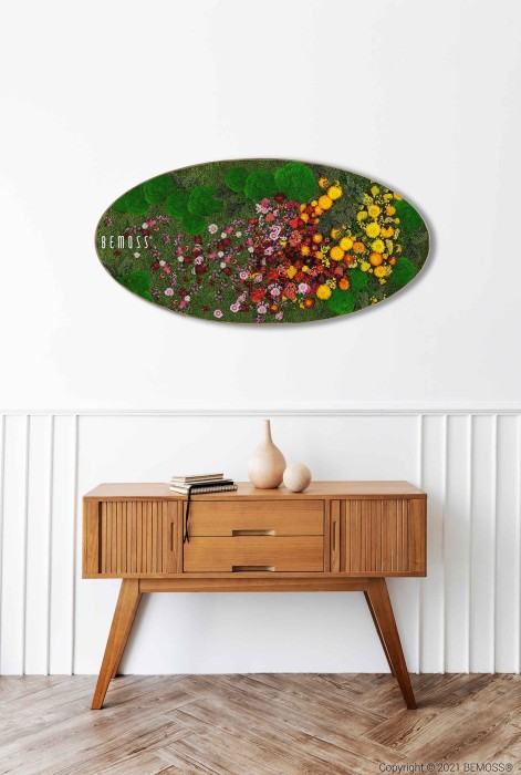 Een modern houten dressoir uit het midden van de eeuw met taps toelopende poten staat tegen een witte muur met lambrisering. Daarboven is een ovaalvormige BEMOSS-mosschilderij gemonteerd met een kleurrijk, abstract bloemdessin. Op het dressoir staan twee vazen en daarop een boek.