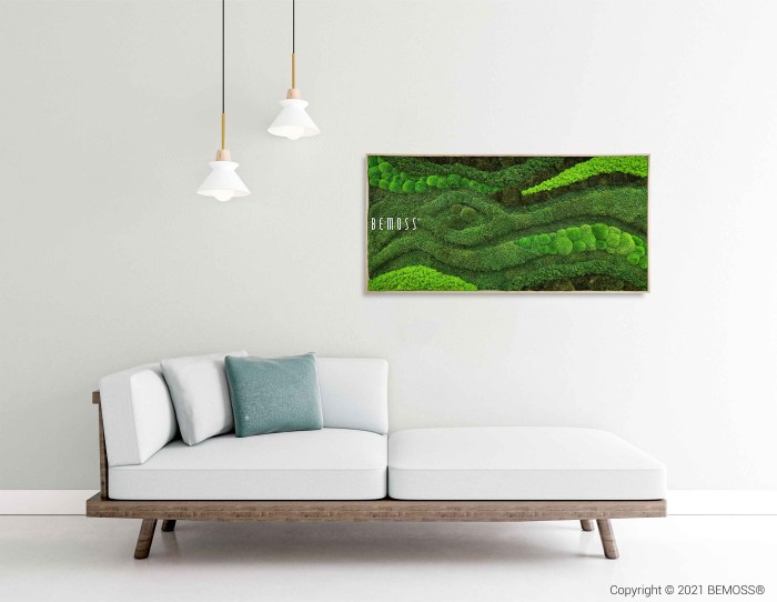 Een moderne, minimalistische woonkamer met een lichtgrijze bank met witte en groene kussens. Aan het plafond hangen twee hanglampen. Aan de lichtgrijze muur is een Mosschilderij BEMOSS® ORTHO TOCÓN in een rechthoekig frame gemonteerd. ©2021 BEMOSS® is zichtbaar in de hoek.