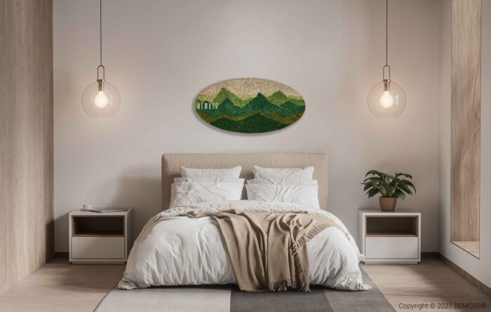 Een moderne slaapkamer met een tweepersoonsbed en wit en beige beddengoed. Boven het bed hangt een groen-bruine BEMOSS-mosschilderij met afbeeldingen van heuvels. Aan weerszijden hangen twee hanglampen en op een nachtkastje rechts staat een potplant. De kamer heeft houten accenten.