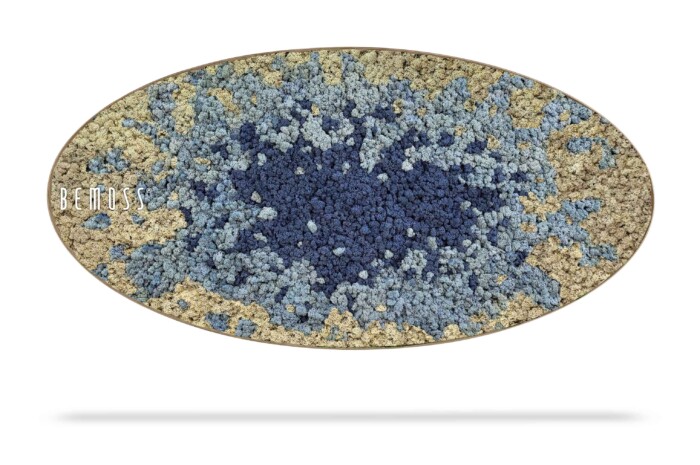 Een ovaalvormig vloerkleed met textuur en een blauw en beige abstract ontwerp. Het middengebied is donkerder blauw en gaat naar de randen toe geleidelijk over in lichter blauw en beige, wat doet denken aan een verstilde moschilderij. Op de linkerkant van het vloerkleed staat in het wit het woord 