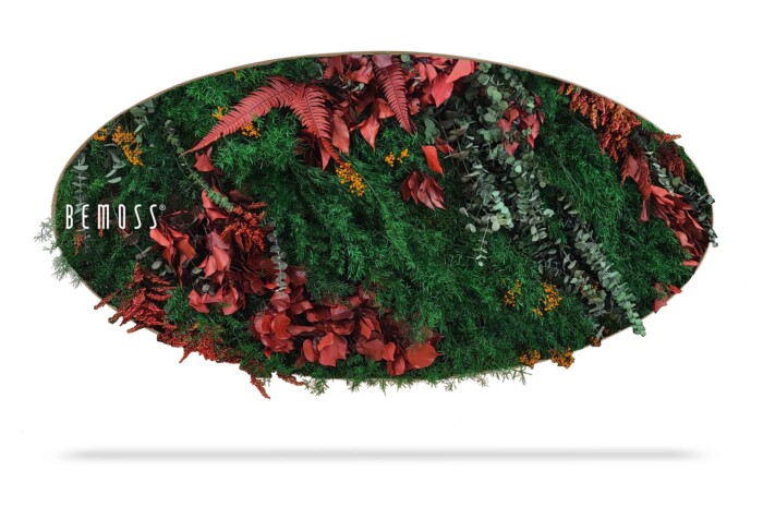 Een ovale wanddecoratie van BE MOSS, oftewel BEMOSS mosschilderij, met een levendig, weelderig arrangement van groen blad en rode bladeren. Het groen vormt een dicht, gestructureerd oppervlak met een organische, natuurlijke uitstraling. Aan de linkerkant is het BE MOSS-logo zichtbaar.