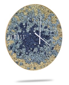 Een Mos klok BEMOSS® SPLASH Sienna met wijzerplaat met een gestructureerd, abstract ontwerp in de kleuren blauw, grijs en beige. De klok heeft dunne witte uren- en minutenwijzers zonder cijfers. Aan de linkerkant van de wijzerplaat is de merknaam "BEMOSS", bekend om zijn prachtige moschilderij-creaties, zichtbaar.