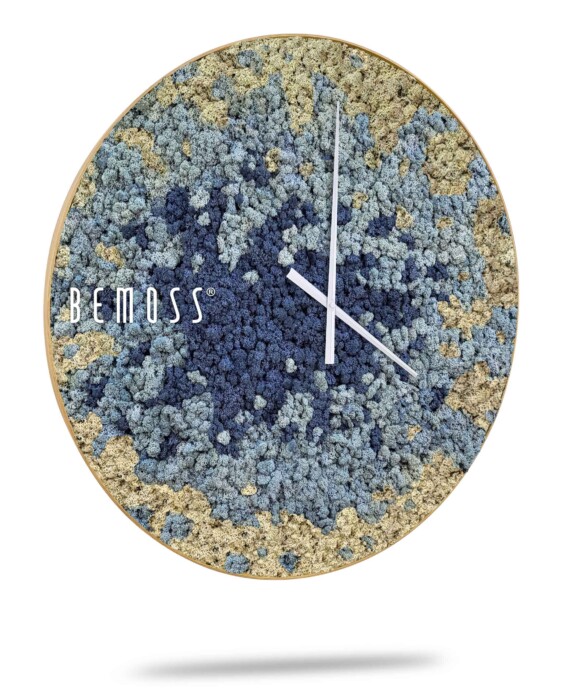 Een Mos klok BEMOSS® SPLASH Sienna met wijzerplaat met een gestructureerd, abstract ontwerp in de kleuren blauw, grijs en beige. De klok heeft dunne witte uren- en minutenwijzers zonder cijfers. Aan de linkerkant van de wijzerplaat is de merknaam 