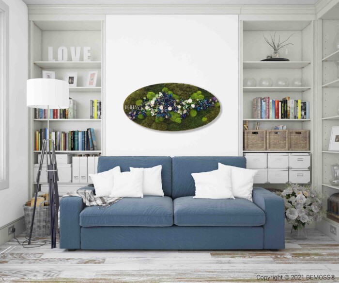 Een moderne woonkamer met een blauwe bank en witte kussens gecentreerd tegen een muur met ingebouwde planken. Boven de bank hangt een ovaalvormige, abstracte bloemenmuurkunst. Er staat een staande lamp aan de linkerkant en verschillende decoratieve items op de planken.