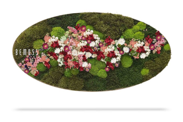 Een ovaalvormig bloemstuk met een mix van groen mos en verschillende bloemen, waaronder rode, roze, witte en paarse bloesems. Het woord 